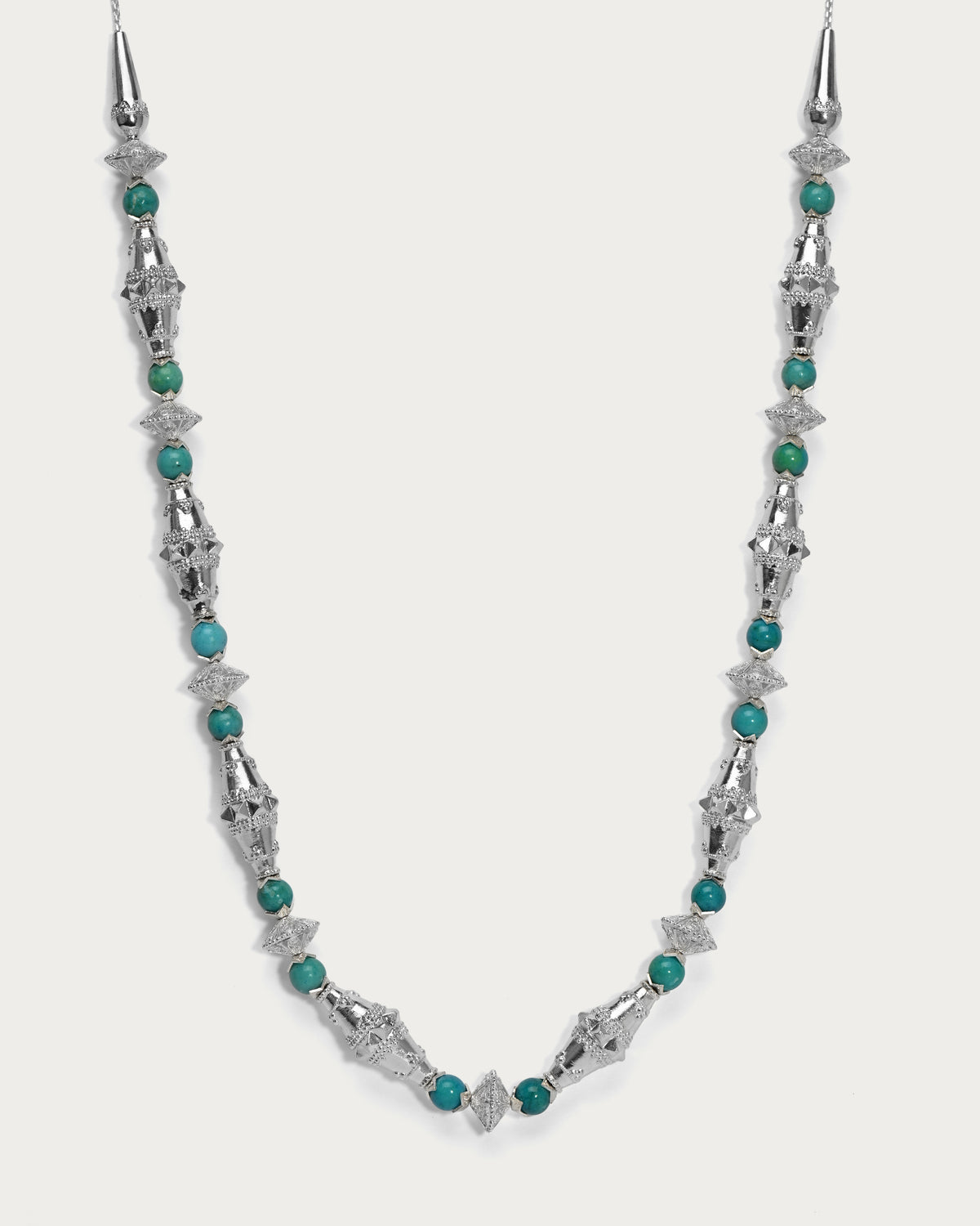 A silver beaded necklace featuring textured metallic starburst links and small round turquoise-green beads, displayed against a light gray background.